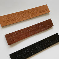 Personalization alphabet, numbers and symbols stamped on natural, cinnamon and black vegetable tanned leather pieces.