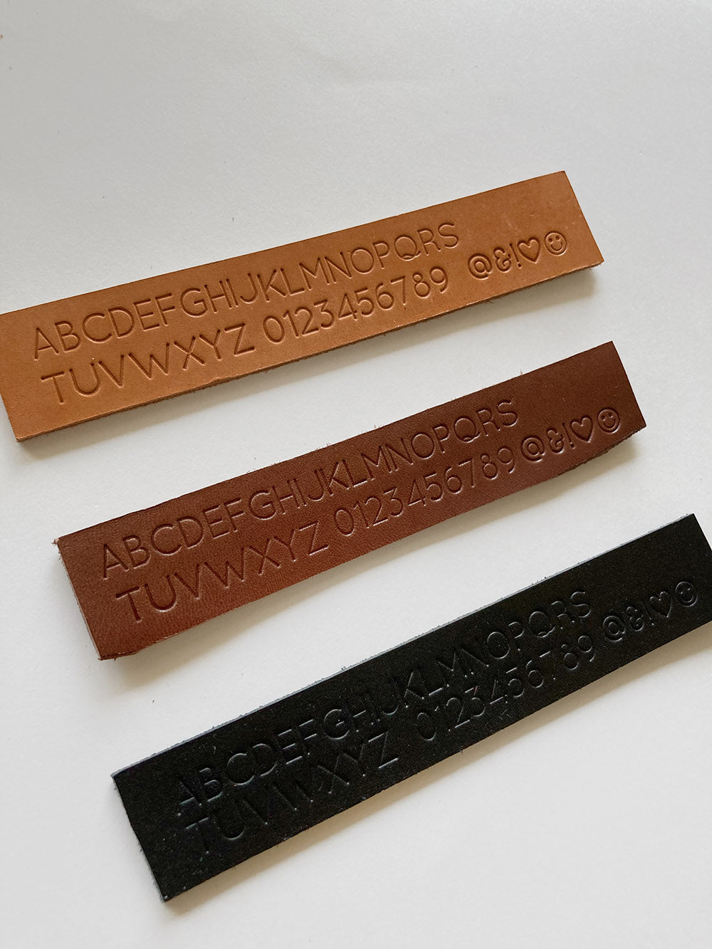 Personalization alphabet, numbers and symbols stamped on natural, cinnamon and black vegetable tanned leather pieces. 